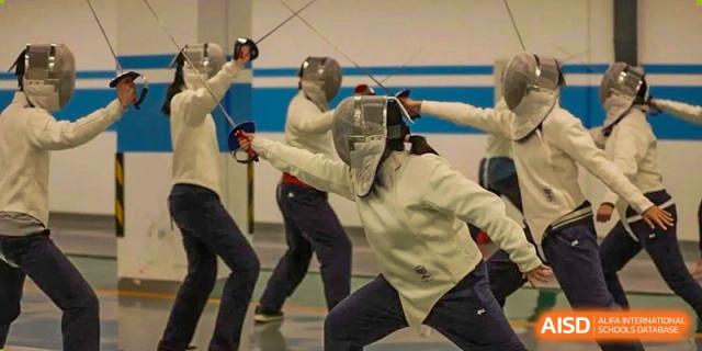Two people engaged in a fencing match, wearing protective masks and white jackets, Beijing Etown Academy International Department