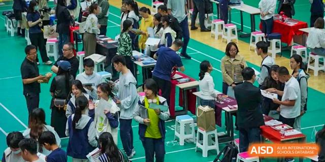 Students gathered around tables and displays at an indoor fair or market event, Beijing Etown Academy International Department