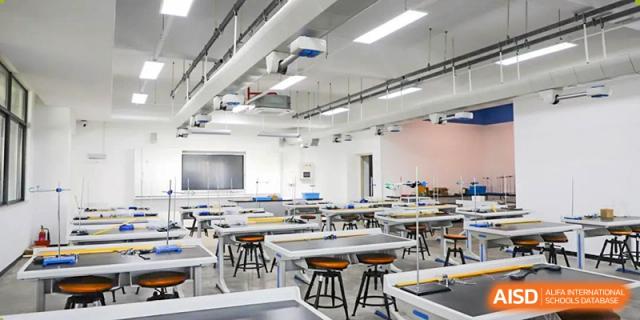 An empty, modern science lab or art classroom at Cogdel Cranleigh School Changsha, featuring long tables, stools, and bright lighting.
