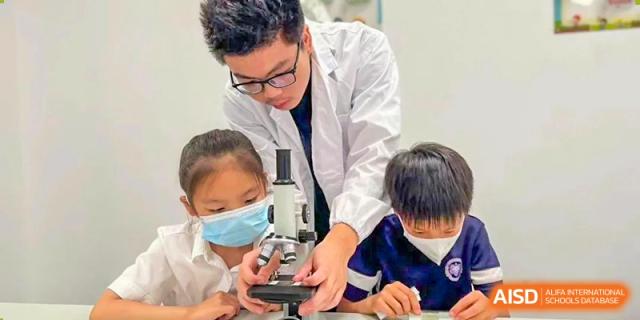 A teacher or instructor at Cogdel Cranleigh School Changsha helping two young students use a microscope in a science class.