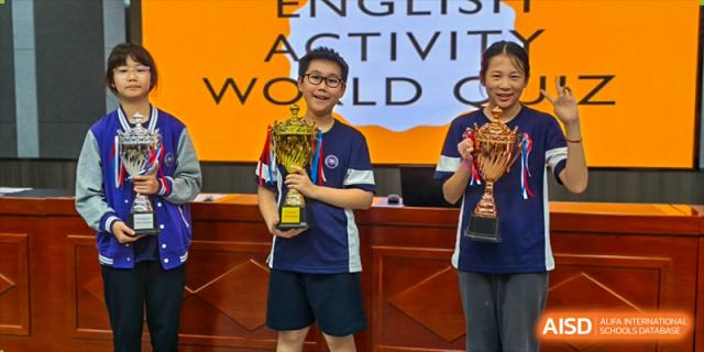 A male student from Cogdel Cranleigh School Changsha standing on stage and proudly holding a trophy after winning an award in a school competition.