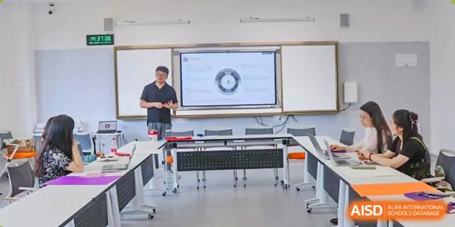 A teacher at Cogdel Cranleigh School Changsha standing and lecturing in a modern classroom with a screen displaying a graphic on the wall.