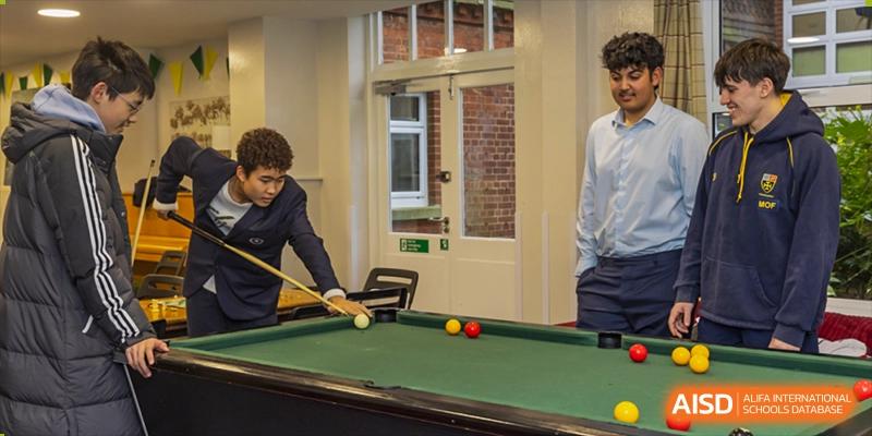 A student from Cogdel Cranleigh School Changsha playing a game of billiards or pool in an indoor recreational area.