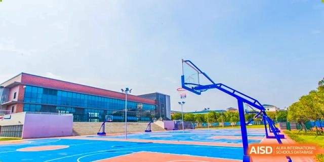 The bright blue and red outdoor basketball court and hoop at Cogdel Cranleigh School Changsha, with the modern school building visible in the background.