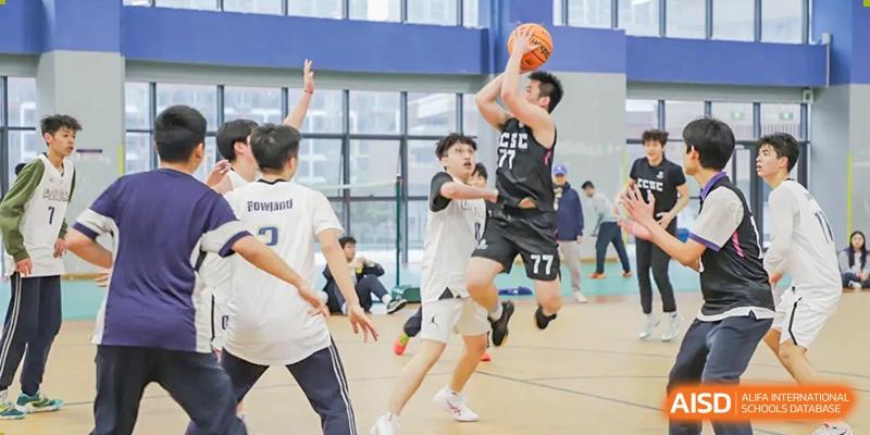 Cogdel Cranleigh School Changsha students intensely playing basketball on an indoor court, with one player mid-air attempting a shot over a defender.