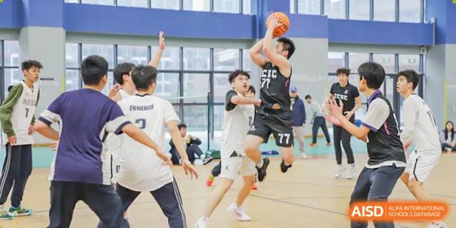 Cogdel Cranleigh School Changsha students intensely playing basketball on an indoor court, with one player mid-air attempting a shot over a defender.