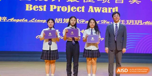 Three female students from Cogdel Cranleigh School Changsha standing on stage in uniform, each holding a Project Award certificate or plaque.