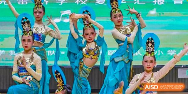 Two young female students from Cogdel Cranleigh School Changsha performing a traditional or cultural dance on stage in bright blue costumes.