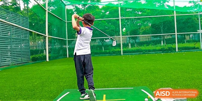 A student from Cogdel Cranleigh School Changsha practicing his golf swing on a driving range or field.