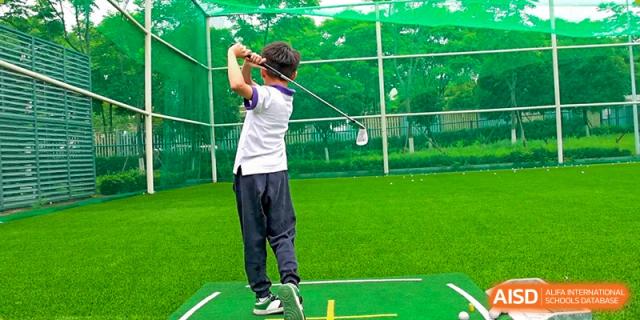 A student from Cogdel Cranleigh School Changsha practicing his golf swing on a driving range or field.