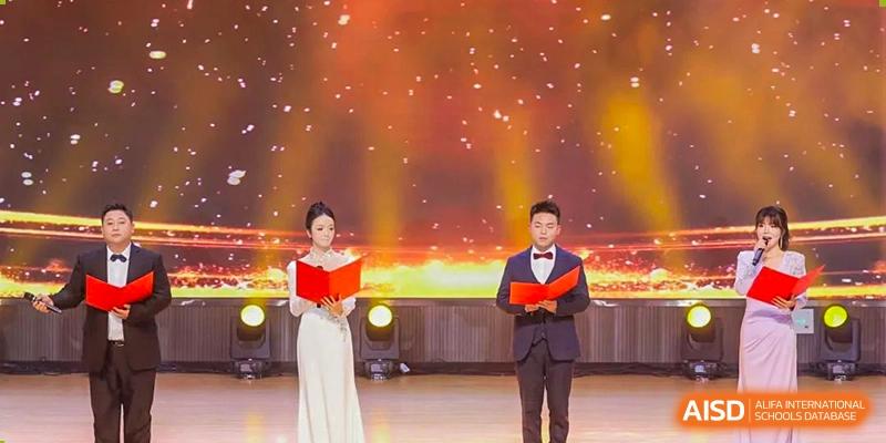 A male and female host or speaker from Cogdel Cranleigh School Changsha standing on a stage during a formal school event, both holding red books.