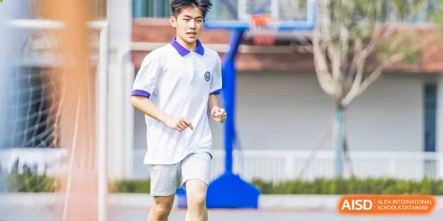 A male student from Cogdel Cranleigh School Changsha in a white uniform shirt running on the outdoor track or sports ground during a physical education activity.