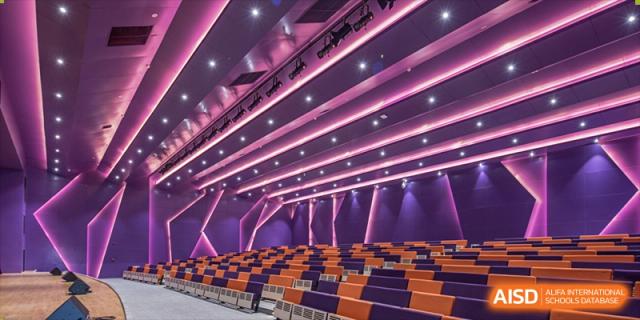 The modern auditorium or lecture hall at Cogdel Cranleigh School Changsha, featuring tiered seating and dramatic purple ceiling lighting.