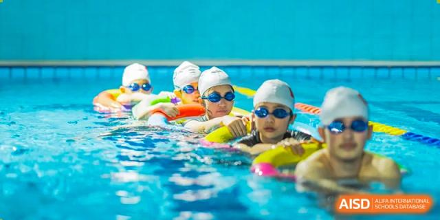 Young students from Cogdel Cranleigh School Changsha in the swimming pool wearing goggles, taking a lesson with flotation aids.