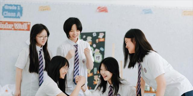 A group of smiling students from Cogdel Cranleigh School Changsha wearing school uniforms and posing for a candid photo in a classroom setting.