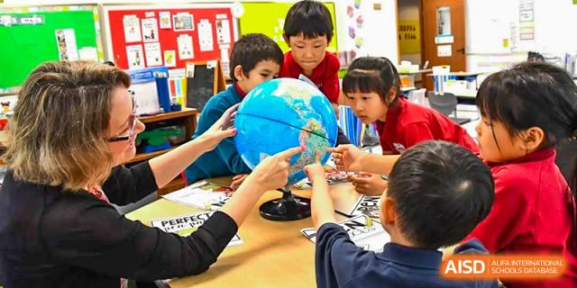 Young AISB-Hope International students gathered around a table, actively learning about geography using a large globe.