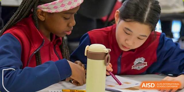 An AISB-Hope International student focused on writing or drawing at a table during a class or activity.