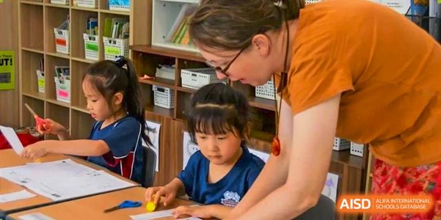A teacher at AISB-Hope International assisting a young student with a writing or craft activity one-on-one.