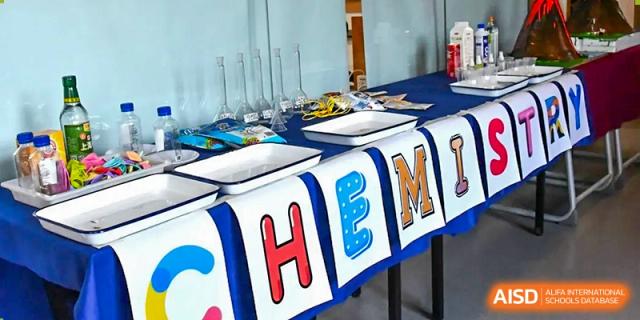 A decorated table set up for a school event at AISB-Hope International, featuring a colorful banner that spells out "HEM" or similar letters.