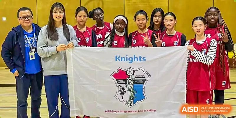 Female students from AISB-Hope International posing with their "Knights" basketball team banner before a game.