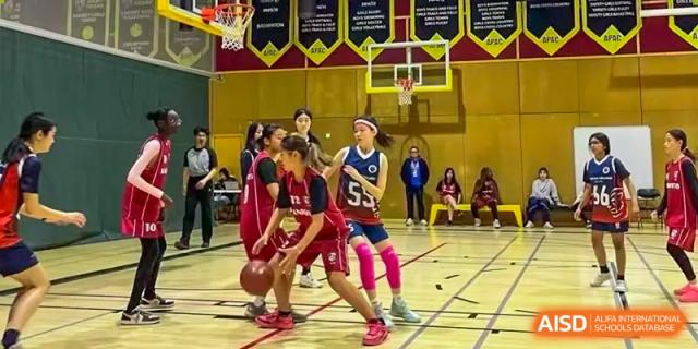 AISB-Hope International students playing an indoor basketball game, with players in red and blue jerseys competing for the ball.