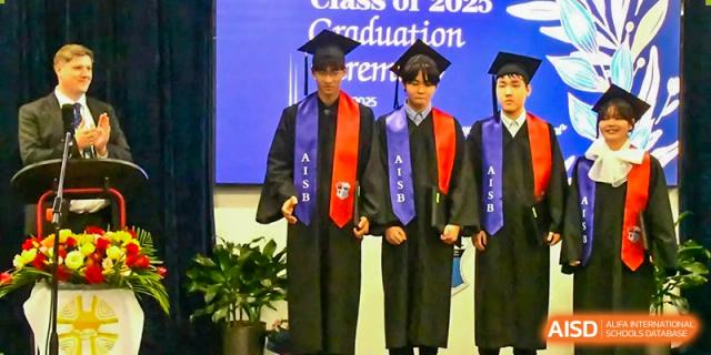 Two AISB-Hope International students in graduation gowns and caps, wearing graduation sashes.