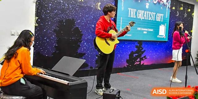 An AISB-Hope International student playing an acoustic guitar on stage during a performance.