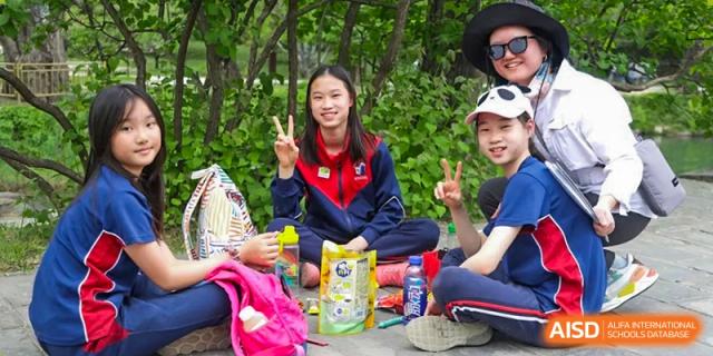 AISB-Hope International students relaxing outdoors, enjoying a break with snacks and giving the peace sign.