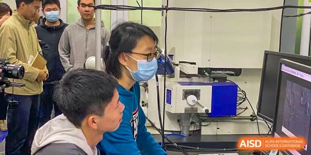 A female teacher wearing a face mask assisting a student with work in a laboratory setting at The Affiliated High School of Peking University's Dalton Academy.