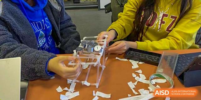 Students from The Affiliated High School of Peking University's Dalton Academy collaboratively building a hands-on project, assembling clear plastic components and small paper notes.