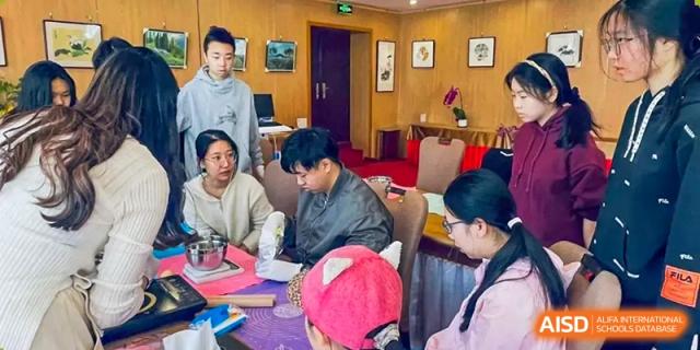 Students from The Affiliated High School of Peking University's Dalton Academy participating in a small group discussion or activity session in a formal room.