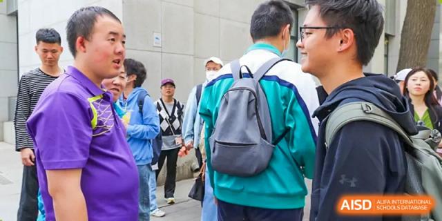 A student from The Affiliated High School of Peking University's Dalton Academy wearing a backpack and speaking with another student outdoors.