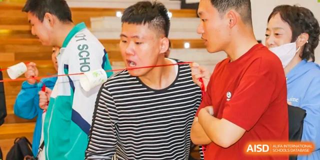 A male student from The Affiliated High School of Peking University's Dalton Academy in a striped shirt participating in an outdoor or indoor hands-on activity.