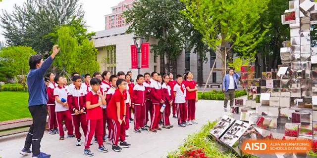 A line of students from The Affiliated High School of Peking University's Dalton Academy dressed in matching red and white uniforms waiting in a queue outdoors on the school campus.