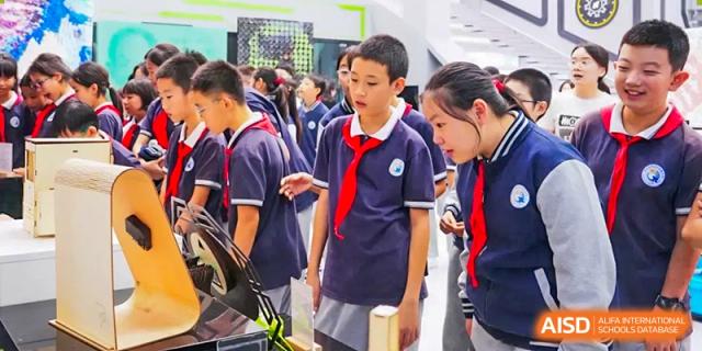 A group of students from The Affiliated High School of Peking University's Dalton Academy wearing school uniforms and engaging in a discussion in a hallway.
