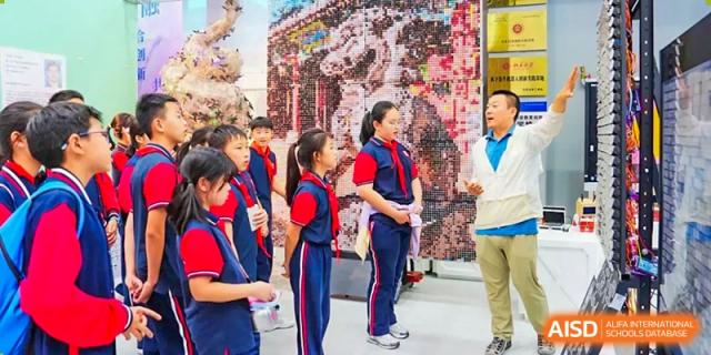 Students from The Affiliated High School of Peking University's Dalton Academy in red and blue uniforms engaging in a discussion in a room with a decorative wall.