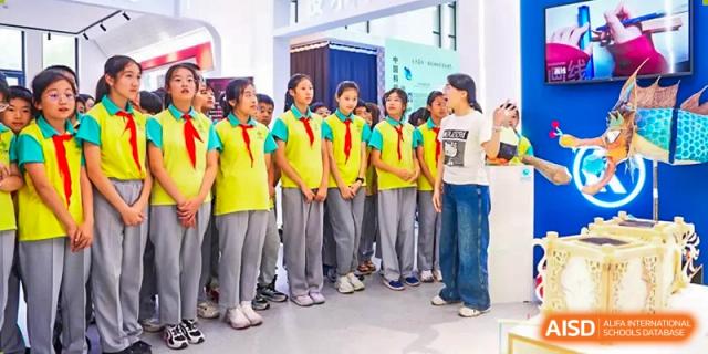 A group of students from The Affiliated High School of Peking University's Dalton Academy wearing matching yellow and green vests, standing together in a line indoors.