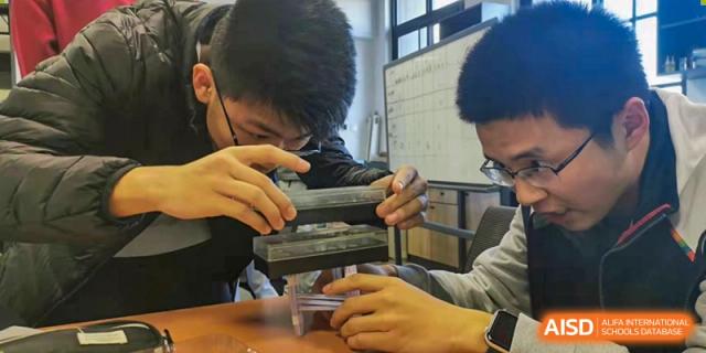 A student from The Affiliated High School of Peking University's Dalton Academy closely examining a small sample or object held in their hands, possibly using a magnifying lens.
