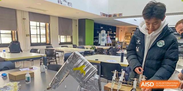 A bright classroom or makerspace at The Affiliated High School of Peking University's Dalton Academy, featuring student projects like a large wooden structure in the foreground.