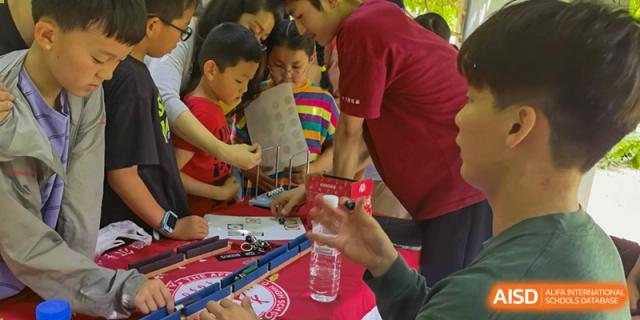 Students and a teacher from The Affiliated High School of Peking University's Dalton Academy collaborating on a close-up, hands-on science or engineering activity at a table.