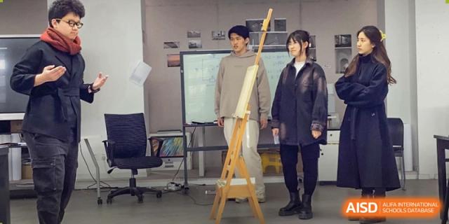 Two students standing next to an easel and a canvas, posing in an art studio or classroom at The Affiliated High School of Peking University's Dalton Academy.