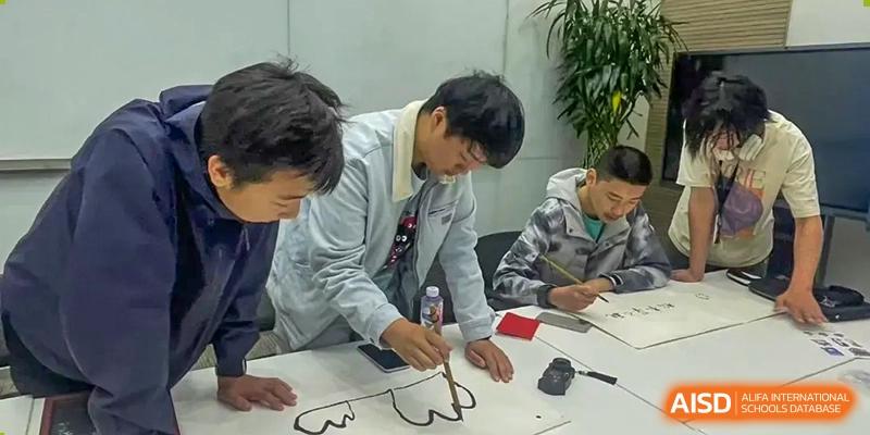 A small group of students collaborating on a painting or drawing project using black ink and brushes on a large piece of paper at The Affiliated High School of Peking University's Dalton Academy.