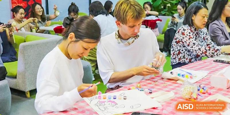 A male student with headphones working on a painting or craft project using small colorful bottles of paint and brushes at The Affiliated High School of Peking University's Dalton Academy.