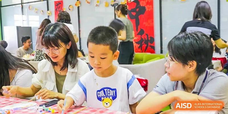 A young boy focused on a craft or art activity, possibly painting or building, during an event at The Affiliated High School of Peking University's Dalton Academy.