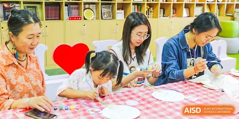 A female student helping a younger child with a hands-on craft project involving painting or gluing small items onto a paper plate at The Affiliated High School of Peking University's Dalton Academy.