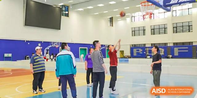 Students from The Affiliated High School of Peking University's Dalton Academy participating in a basketball activity, with one student shooting a ball in an indoor court.