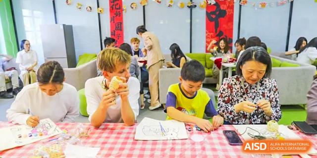 A foreign teacher and a young student from The Affiliated High School of Peking University's Dalton Academy seated at a table with a checked tablecloth, participating in a craft or activity.