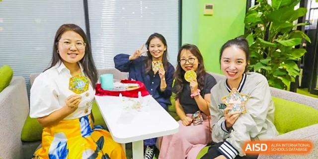 A small group of young women from The Affiliated High School of Peking University's Dalton Academy smiling and posing for a photo while holding up cultural snacks or treats.