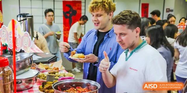A foreign teacher and students from The Affiliated High School of Peking University's Dalton Academy enjoying food at a buffet, with the teacher giving a thumbs-up.
