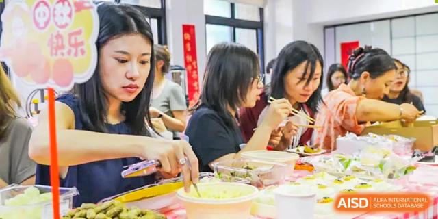 A group of female students and teachers from The Affiliated High School of Peking University's Dalton Academy sitting together and enjoying a meal at a long table.